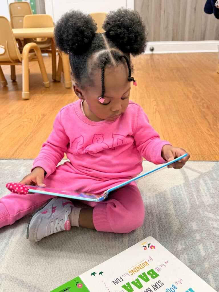 Toddler dressed in pink, reading a book